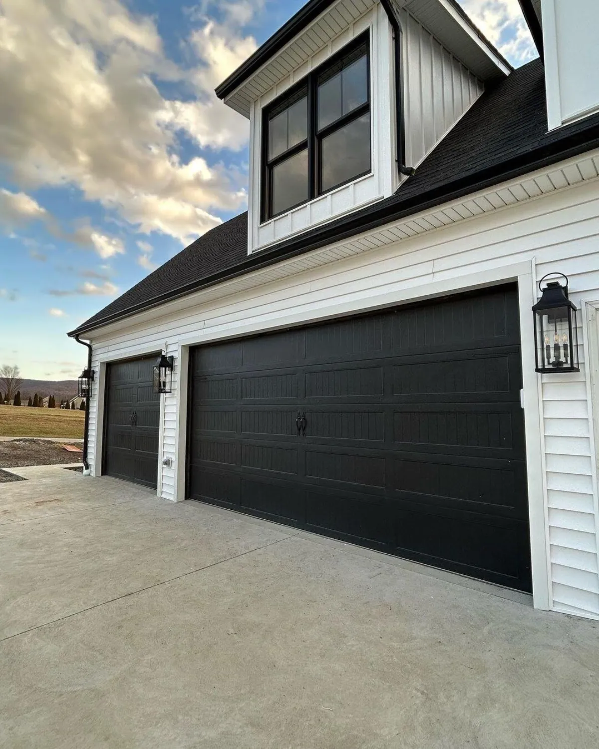 Black stamped carriage house steel door with wood-grain texture on a farmhouse